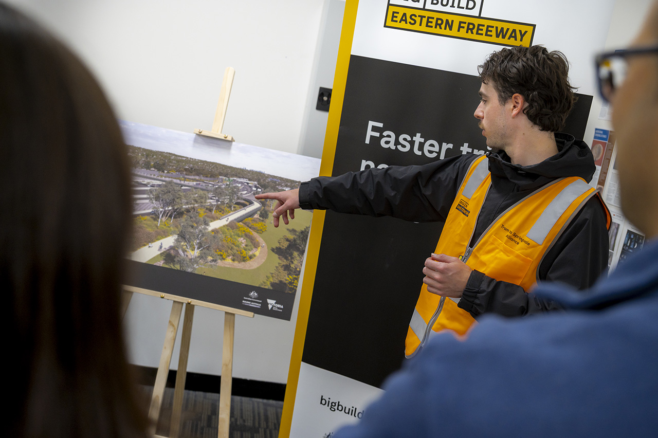 Worker in an orange high visibility vest pointing to a map of the Eastern Freeway Upgrades