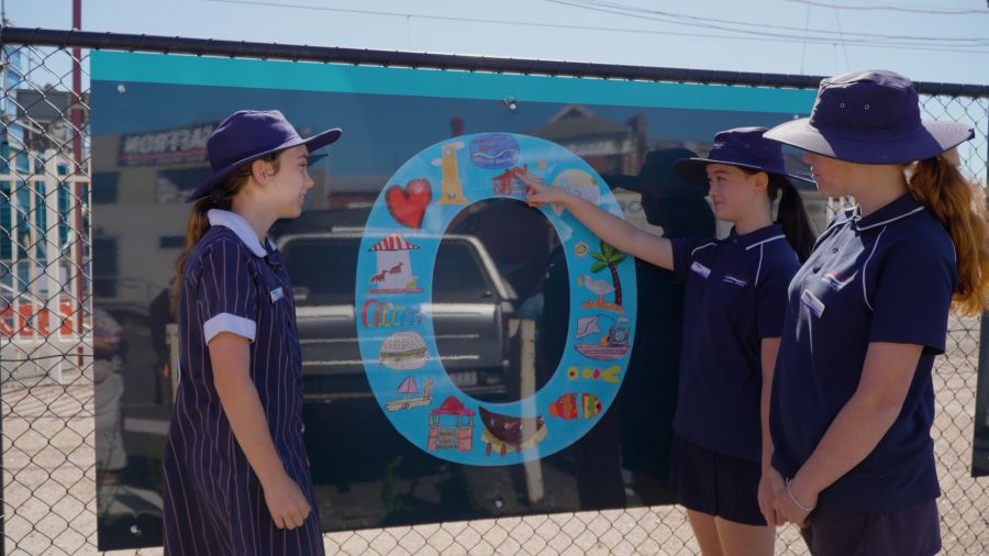 Mordialloc Beach Primary School students Freya, Alina, and Hannah look at some of their artwork in the mural