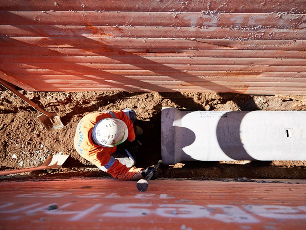 Image displays a birds eye view of a worker in a narrow space alongside a a big pipe