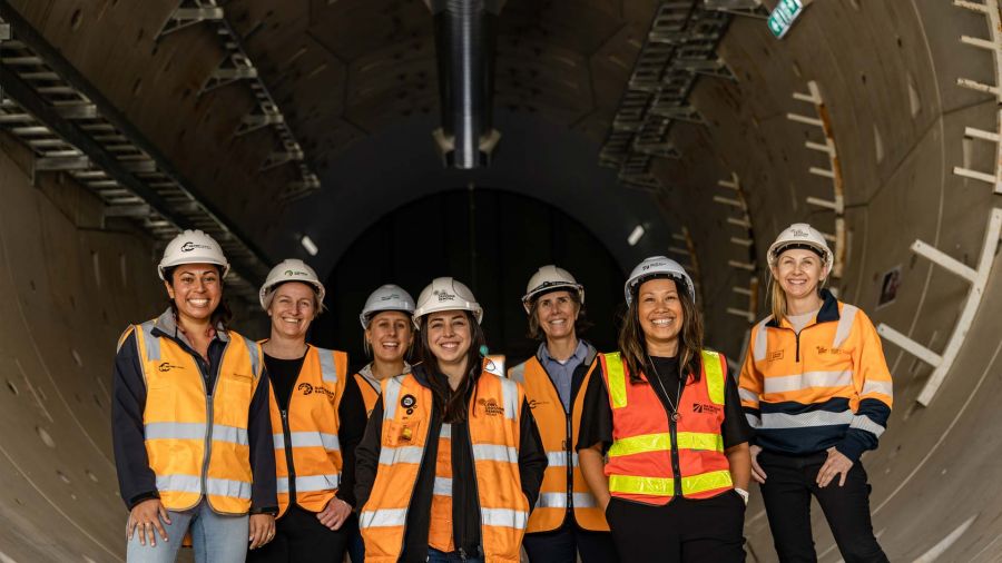 Seven female engineers in hardhats and high-vis clothing stand in a tunnel.