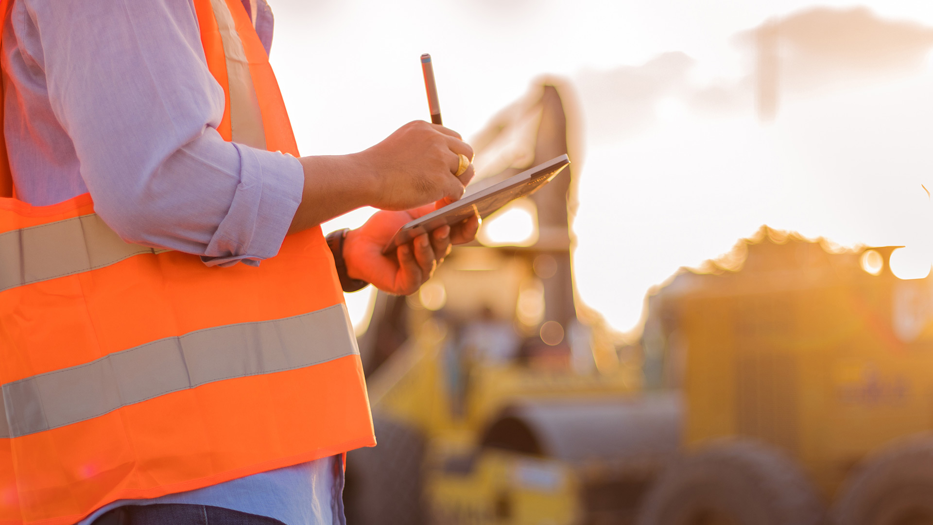 An engineer with hard hat using a computer tablet inspecting and working at a construction site.