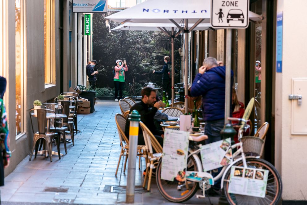 People dine in a laneway in front of an artwork