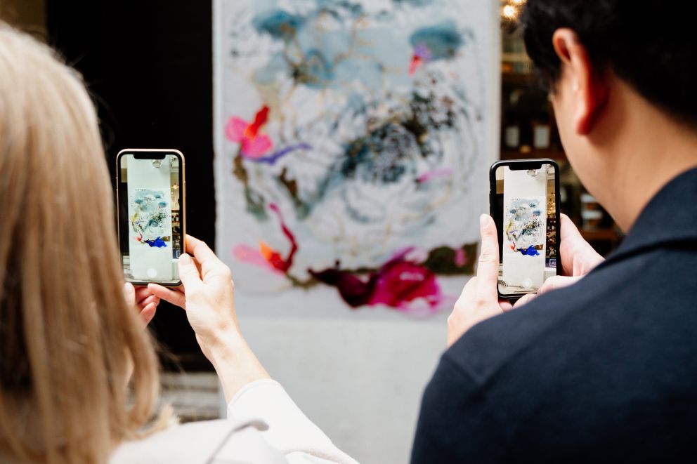 Two people hold phone cameras in front of an artwork