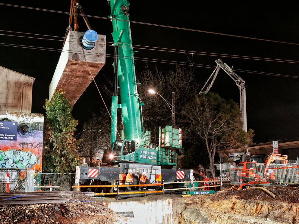 A large crane lifting a concrete beam into the trench.