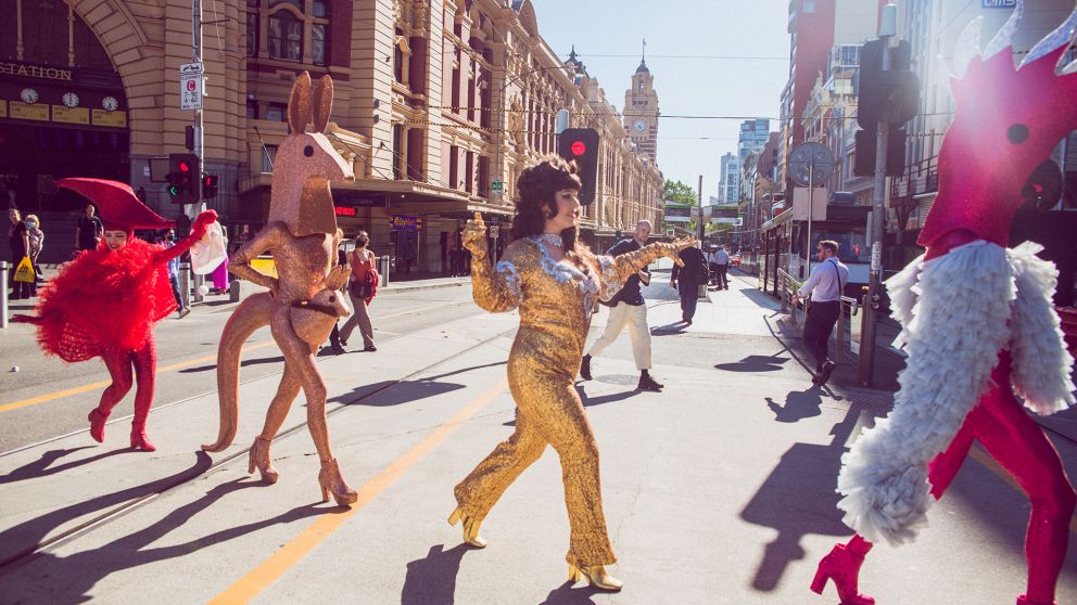People in glittery costumes walk across a main road in Melbourne
