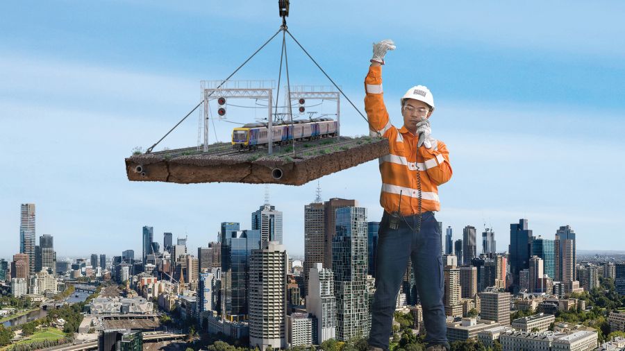A giant construction worker towers over the city as he directs a large crane carrying a train and section of train track 