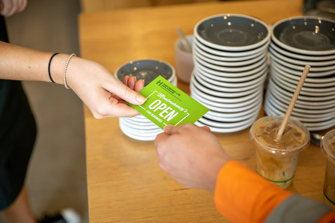 A person at a cafe handing a card that says Montmorency open for business to another person