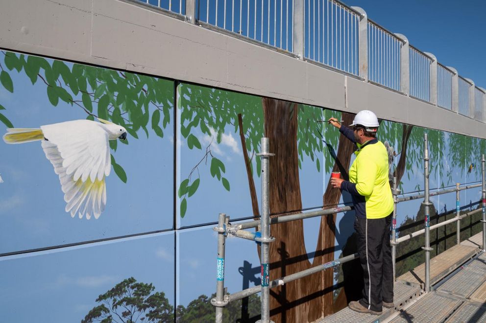 Artist Ervin Molnar painting native tree leaves in to the bridge mural