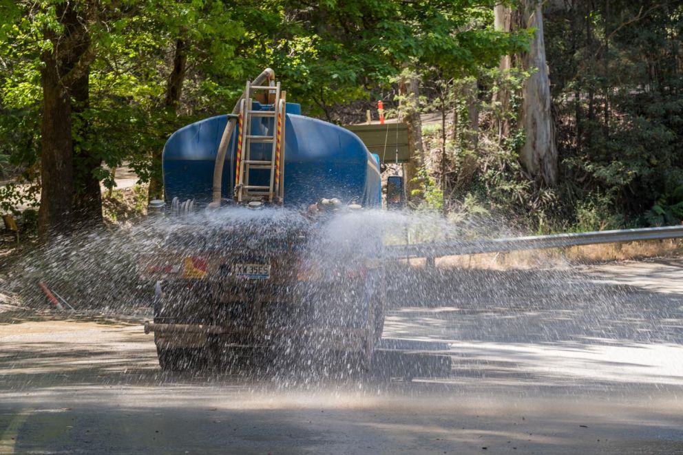 A water truck helps stop dust by dousing the road in water