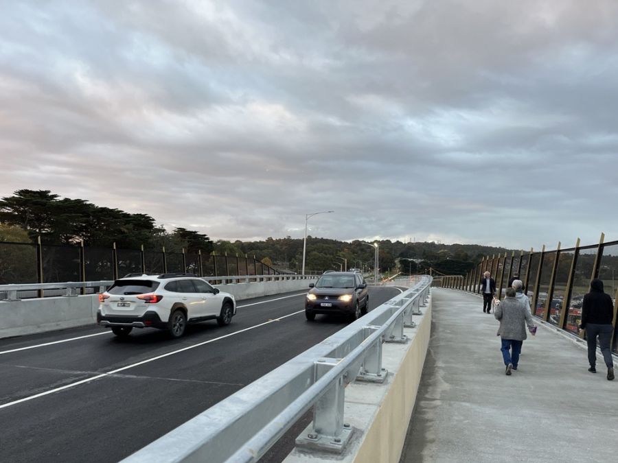 Two cars on new road bridge and pedestrians walking over