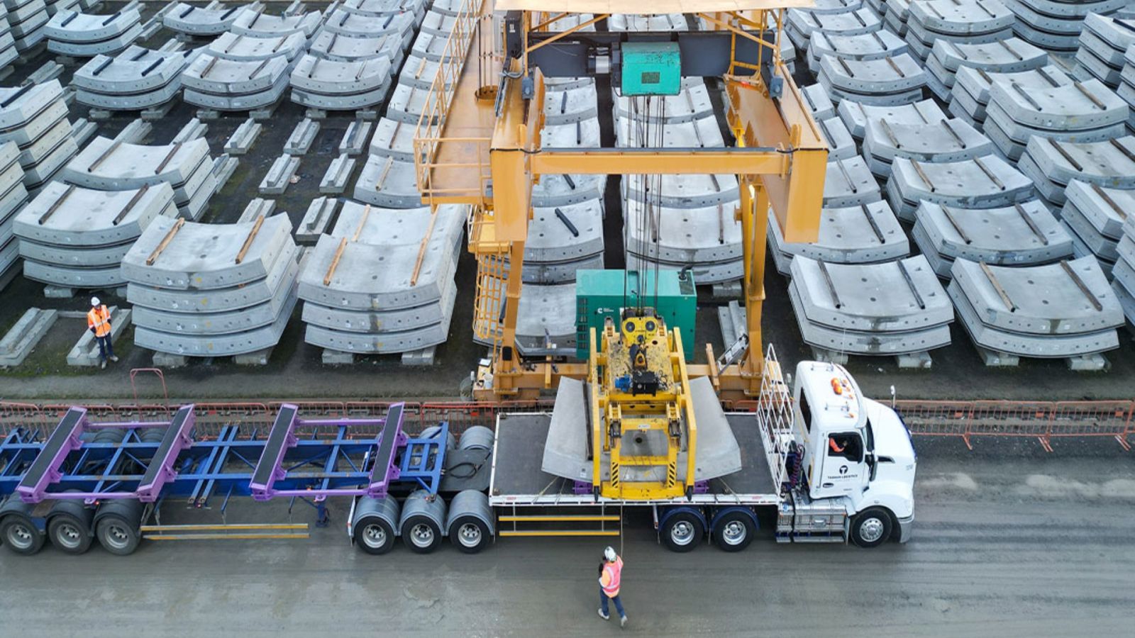 Large concrete segments are being delivered to a large open yard.