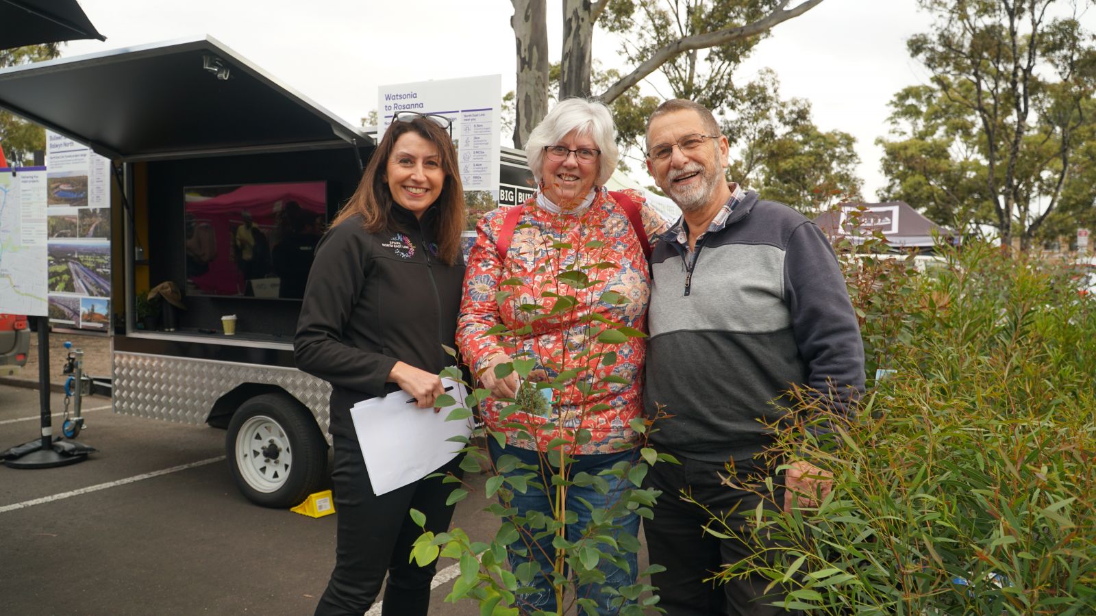 3 people in photo smiling to camera. Plants are in front and to the right.