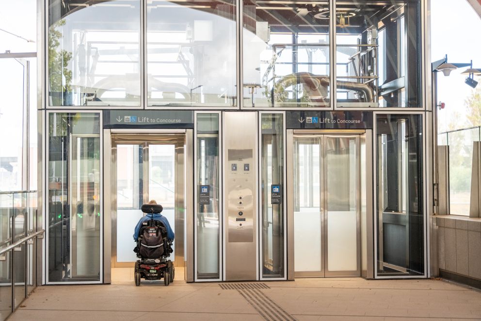 Two glass lifts, with a person in a wheelchair entering one