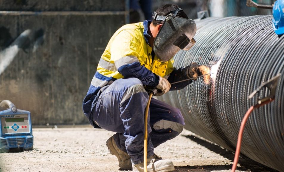 A person wearing protective clothes and a helmet is welding a large pipe