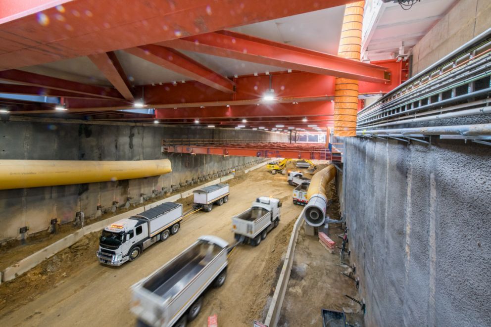 Trucks drive through a large underground construction site.