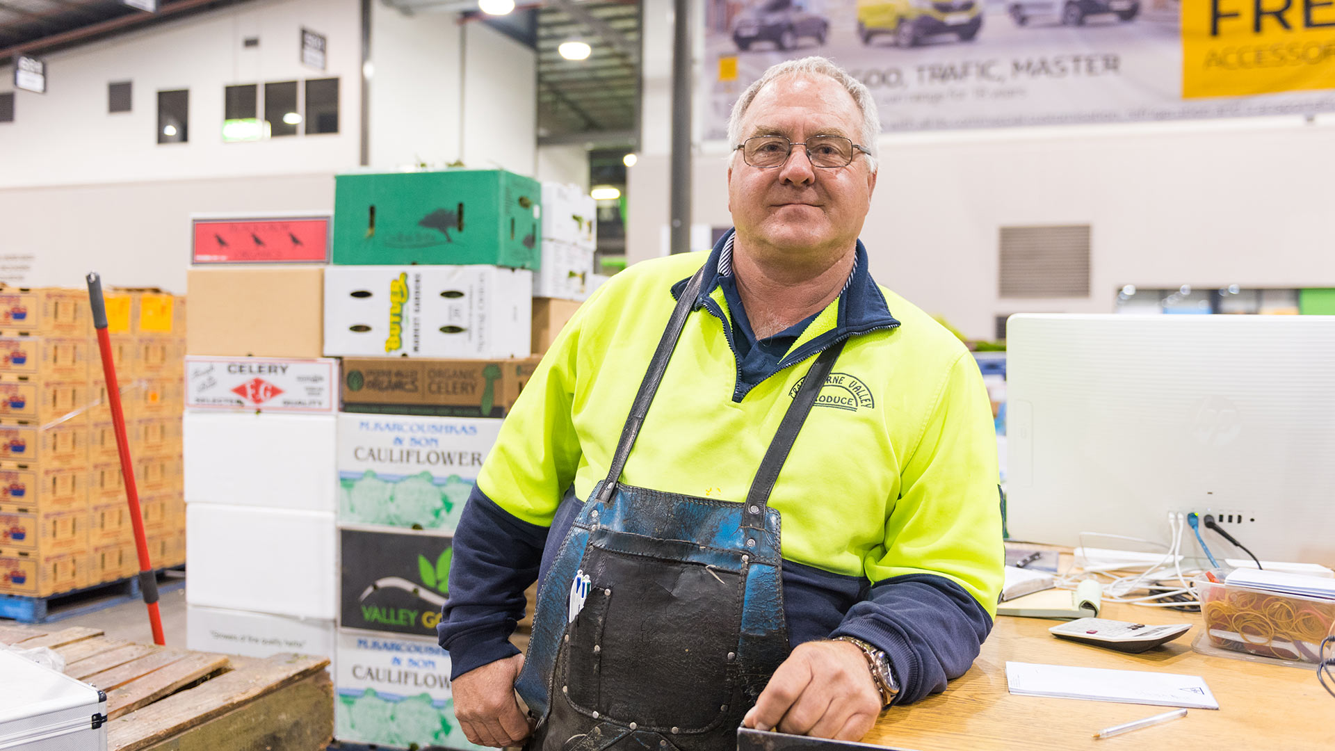 A man wearing a tool apron leaning on a desk in front of boxes.