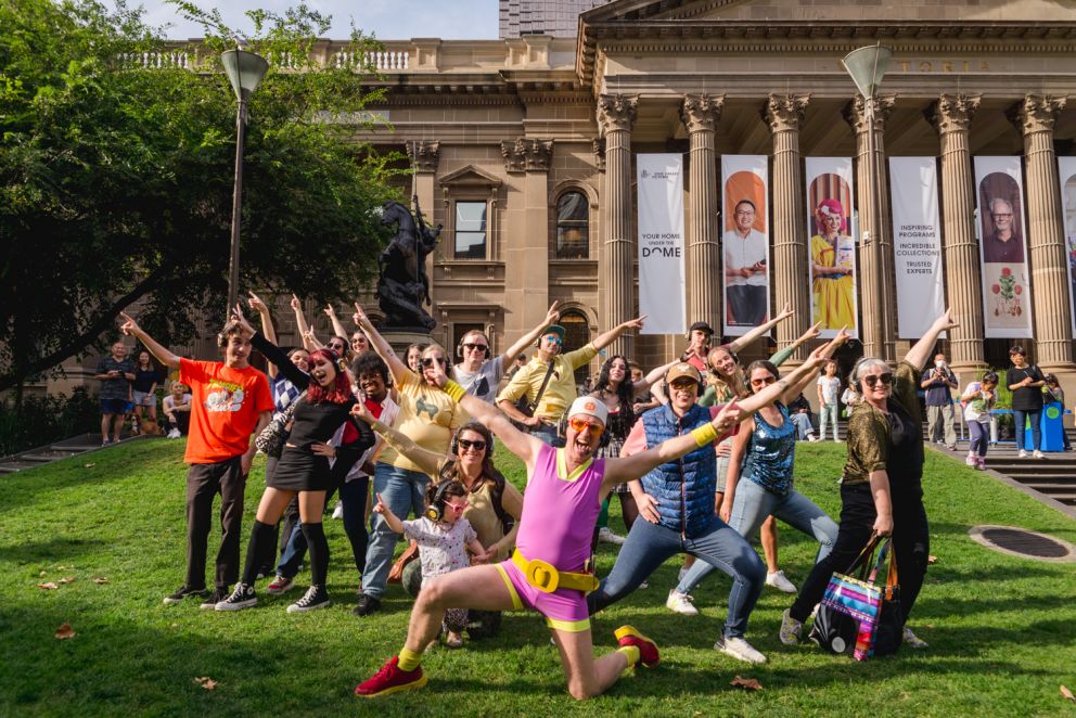 People dressed in colourful outfits wearing headphones pose on the State Library of Victoria lawn