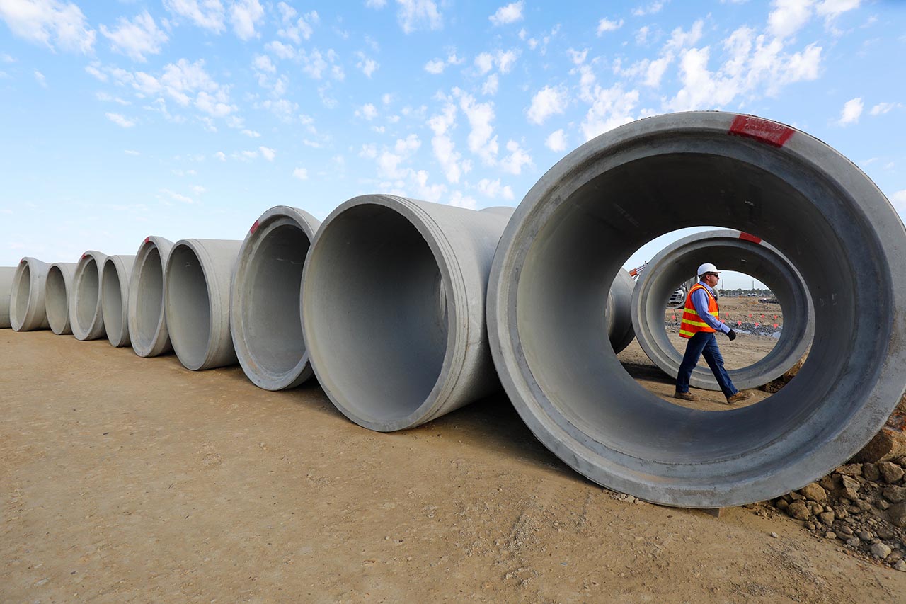 Male construction worker walking between large concrete pipes 