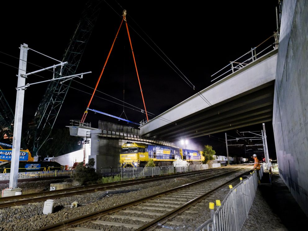 Crane lifting large concrete beam in place for road bridge.