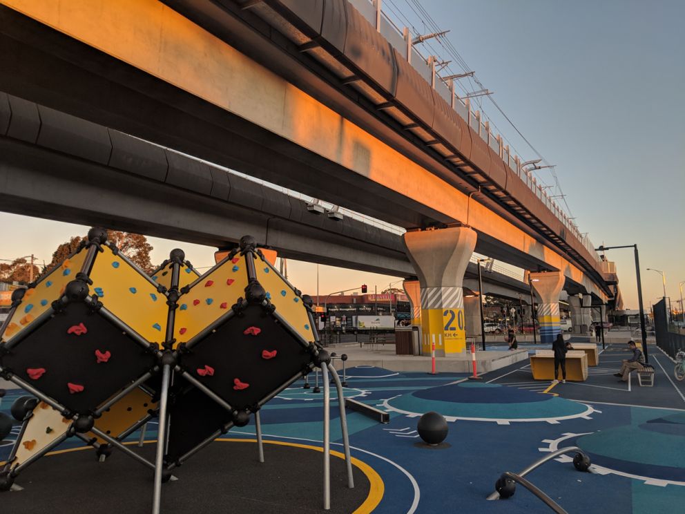 Rock climbing cubes and boulders and table tennis table under an elevated rail bridge.