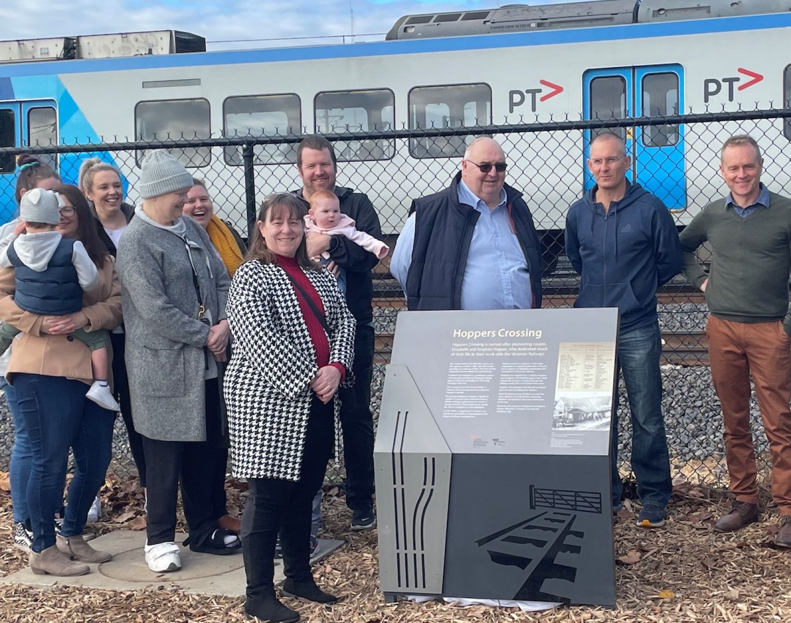 The new memorial marker at Hoppers Crossing Station with a train passing behind
