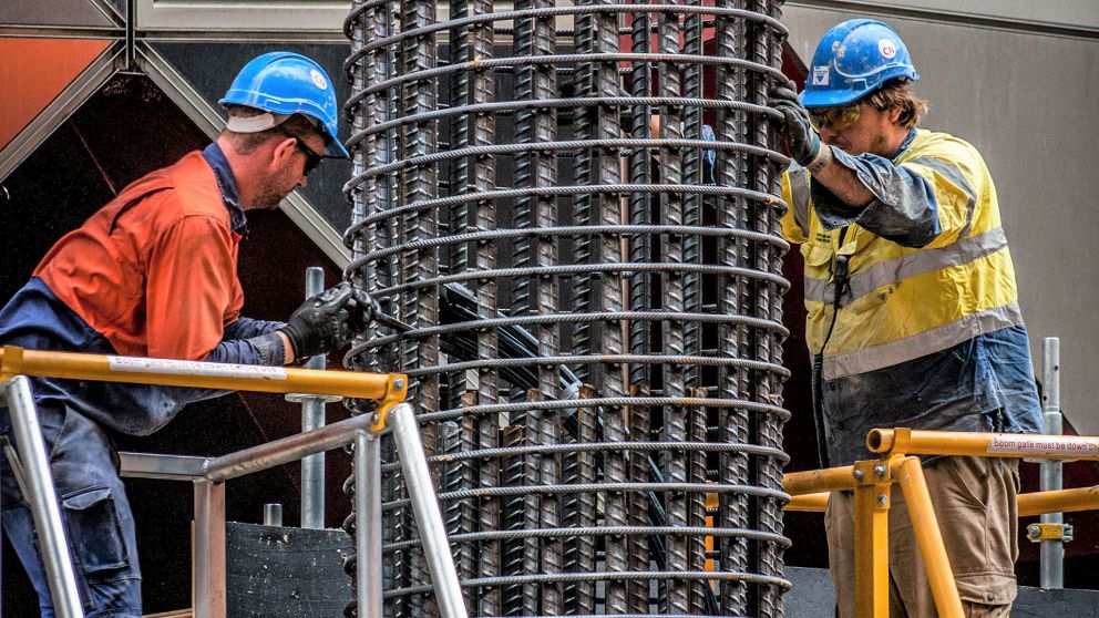 Two workers working on a large circle of metal pipes that runs from above and below them.