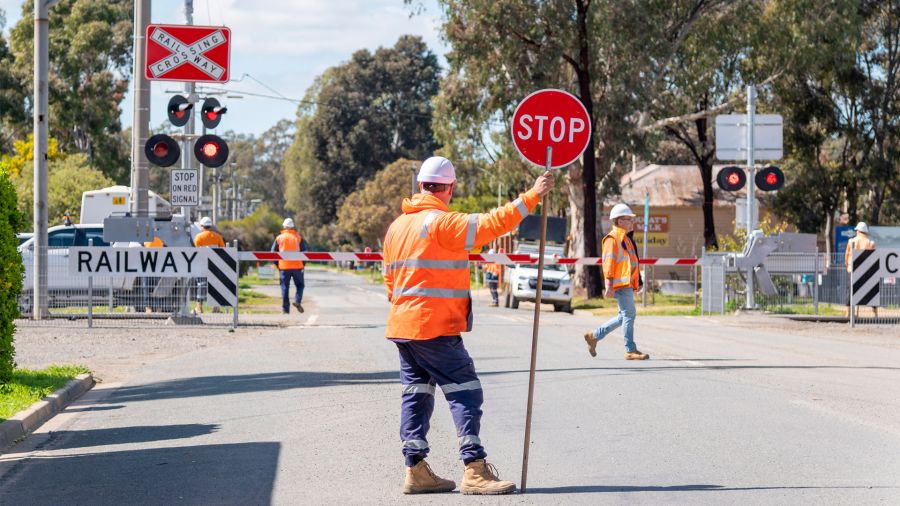 Traffic controller holding stop sign in front of level crossing upgrade