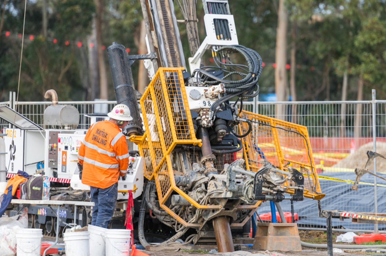 A construction worker wearing high-vis and protective equipment standing next to large drilling machinery. 