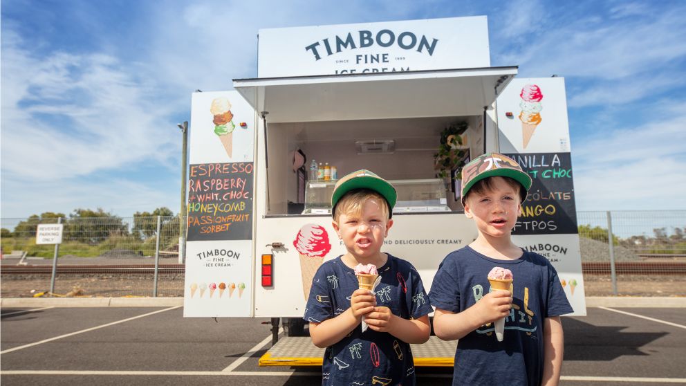 Two children eating ice cream in front of ice cream truck. 