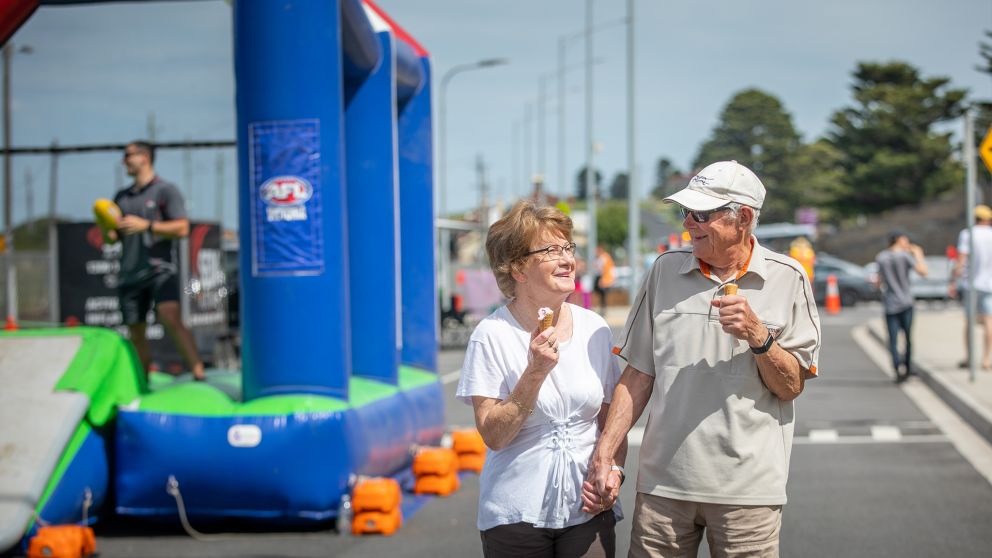 An older couple walk hand in hand eating ice cream. 