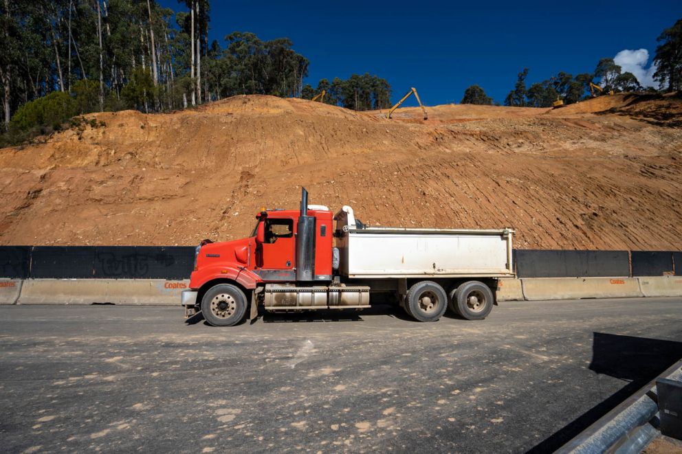 A construction truck drives through the worksite while machinery works on the landslip in the background 14 April