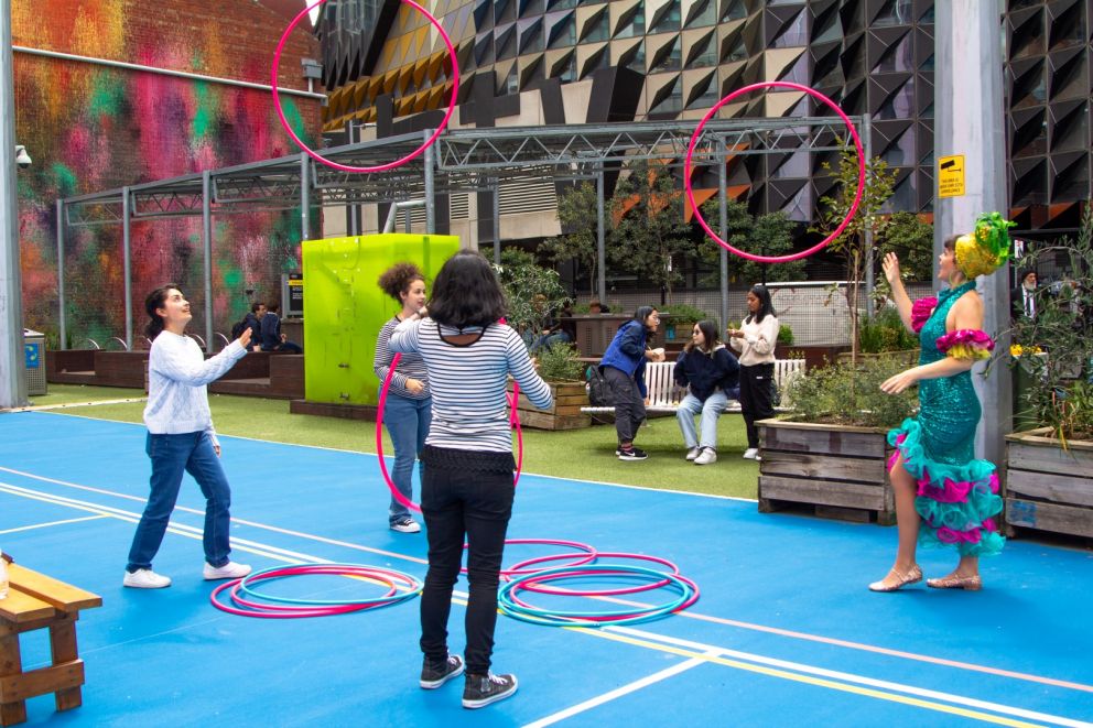 Image of people playing with hoola hoops. Hayley Hoopla is dressed in a blue and pink sequin dress.