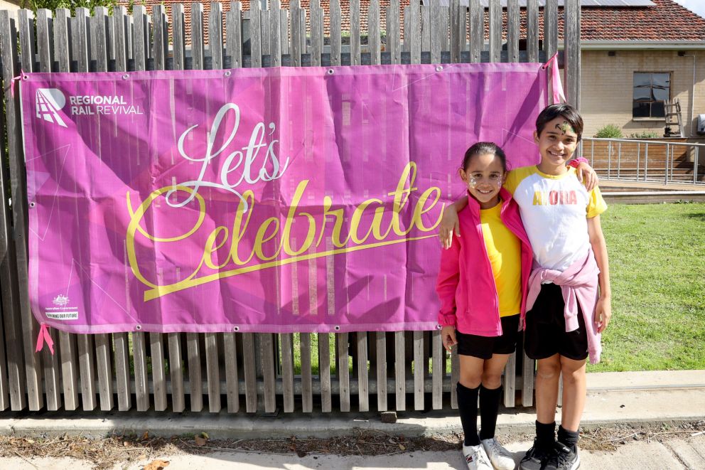 A large pink banner with the words 'Let's celebrate' and two children standing beside it smiling