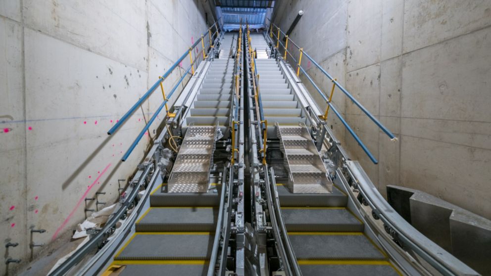 A set of escalators being installed in a underground, concrete station.