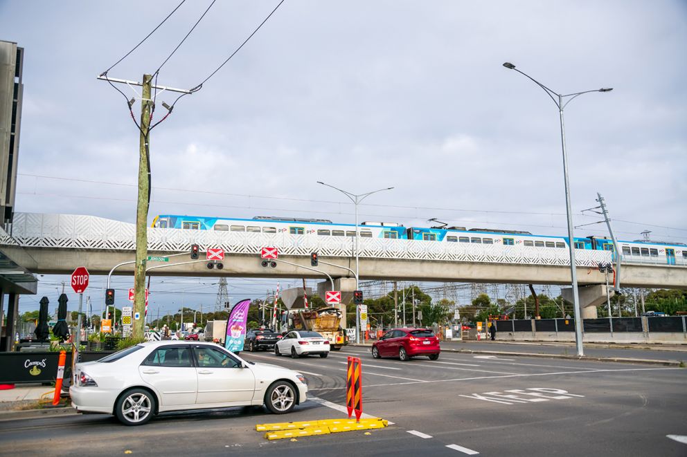 A train on the city bound rail bridge over Keon Parade with traffic stopped at the level crossing