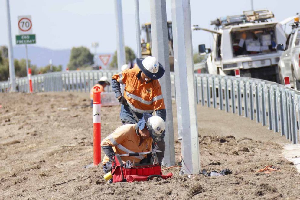 New streetlights being installed along the side of the widened freeway ramp.