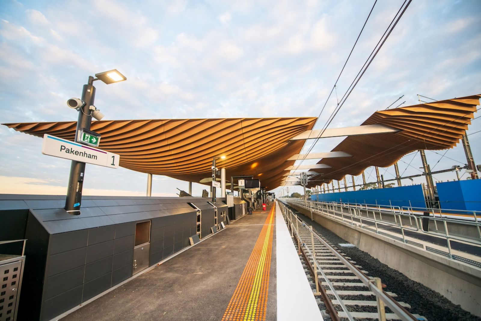 An elevated train platform with a yellow, wavy roof. A sign says Pakenham, platform 1.