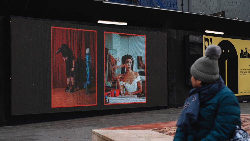 A person in a blue jacket with a grey beanie looks at images of artwork on a screen 