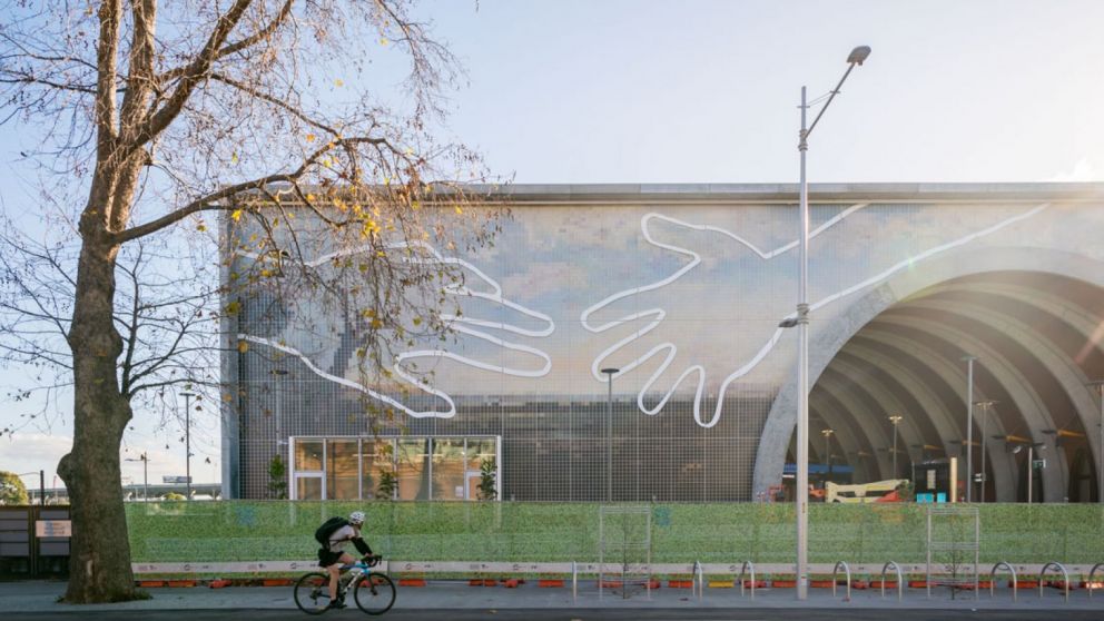 A wide shot of Arden featuring a cyclist looking at Abdul Abdullah's 'Come Together' artwork. 