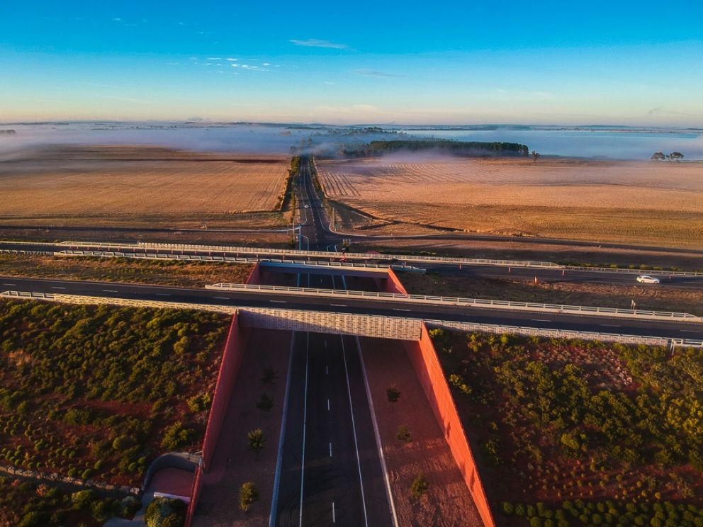 Aerial view of a section of the Western Highway, looking into an underpass. Clouds hang low over a paddock in the distance.