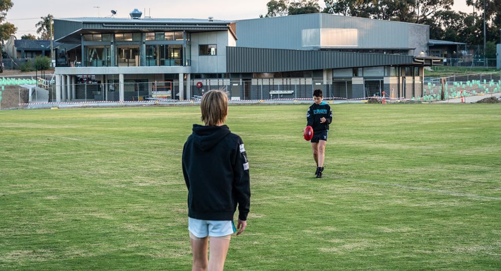 Two young boys kicking an AFL football on the oval at Greensborough College with the new pavilion in the background.