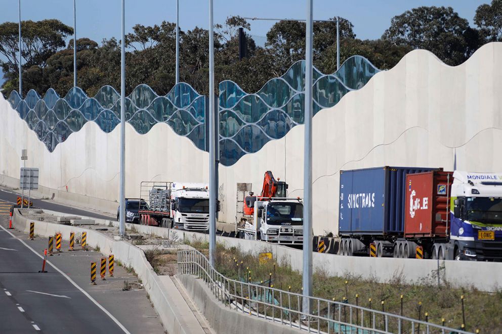 Photo of trucks on the West Gate Freeway with completed sections of new noise walls in the background