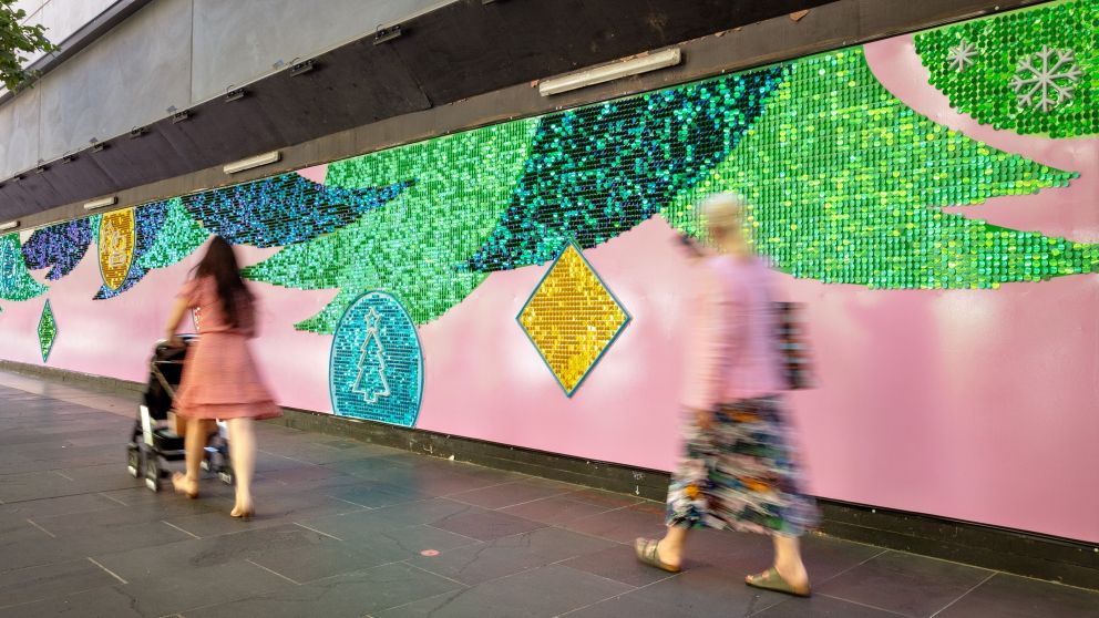 People walk past a colourful mural with shimmering Christmas trees.