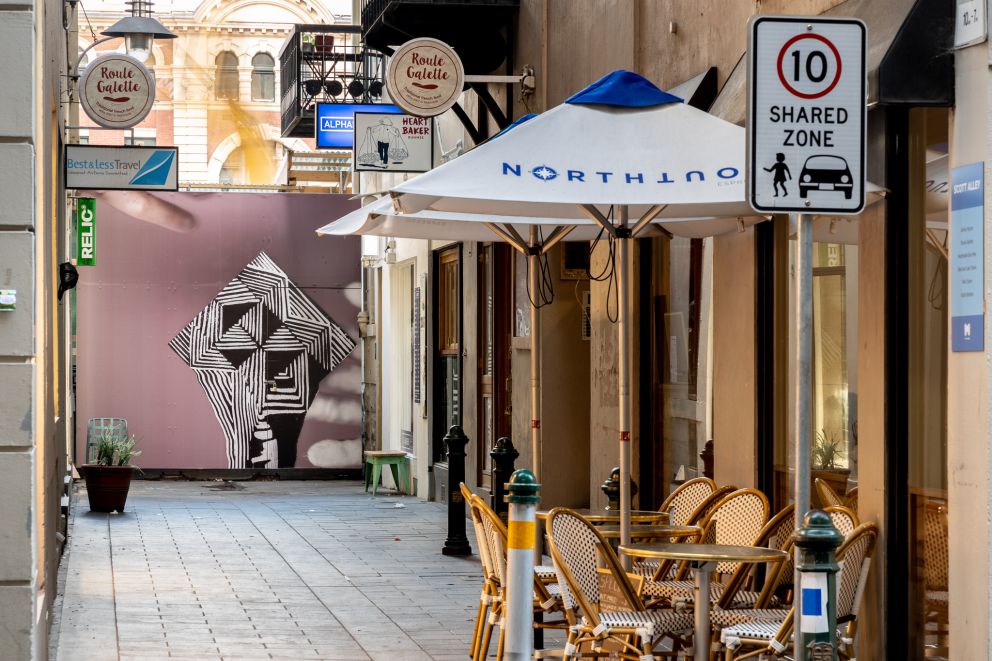 Artwork at the end of an alleyway with cafe tables in the foreground