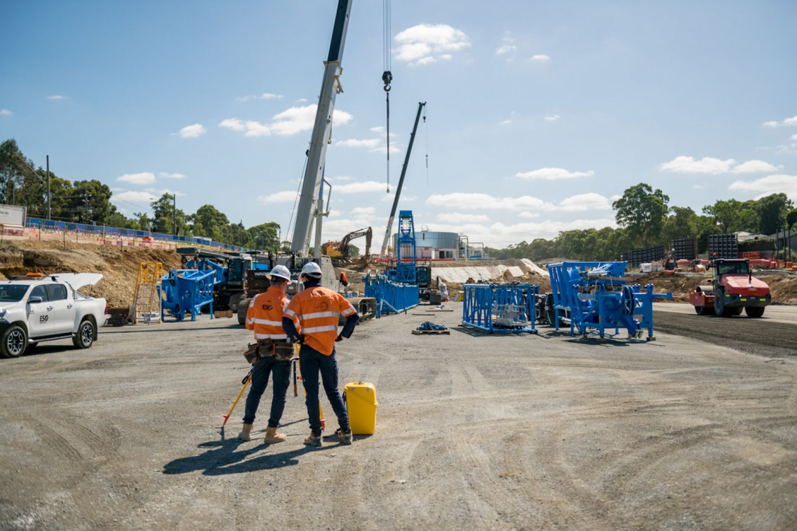 Workers stand on a construction site in front of two cranes.