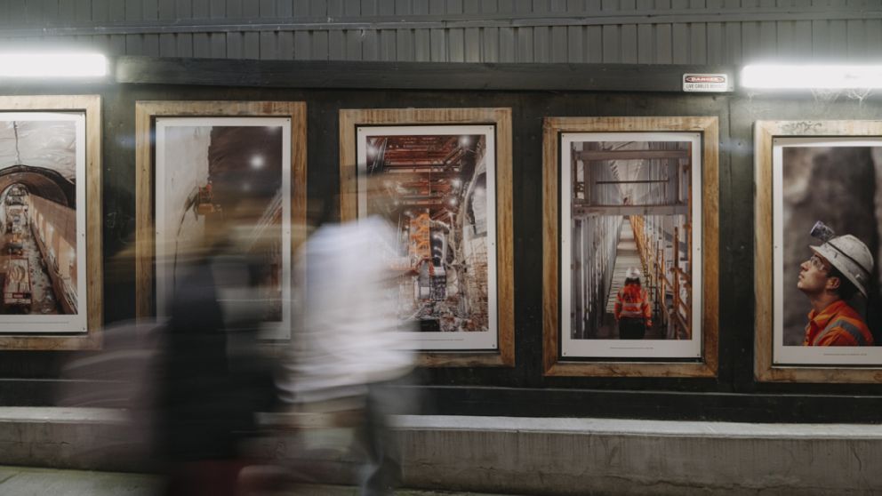 Image of people walking past 5 wooden frames containing images of Metro Tunnel construction. 