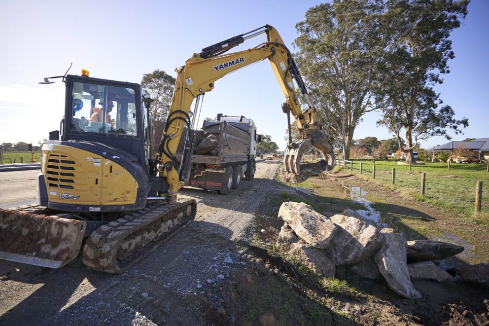 An excavator operator carefully selecting a boulder for rock beaching preparation