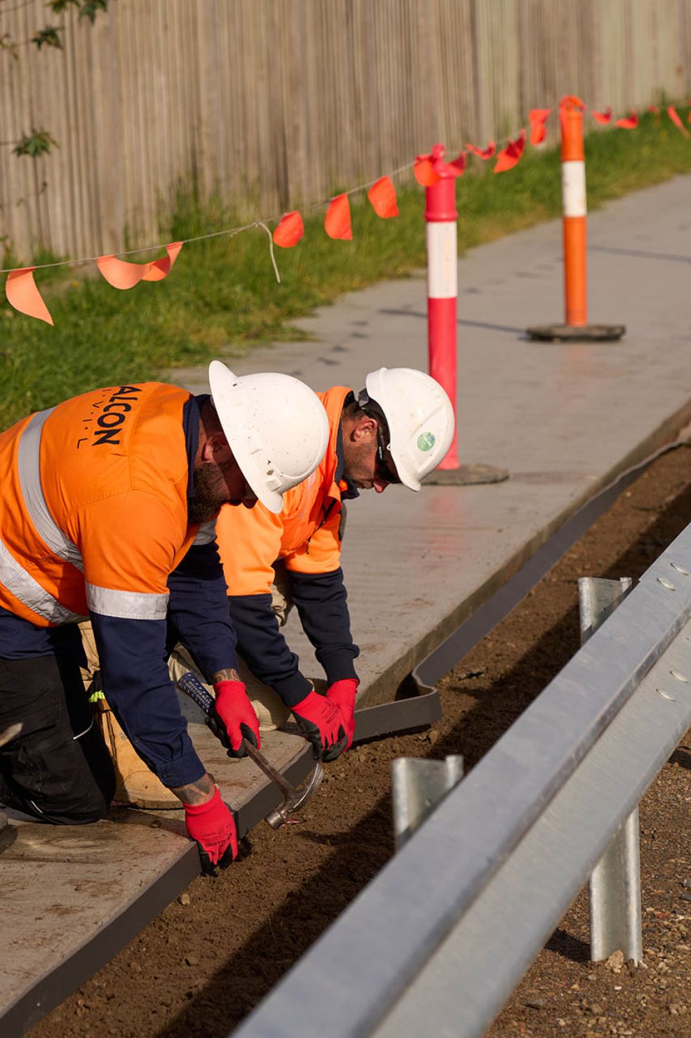 Two workers carefully installing Ableflex, a material that creates the joint between the shared use path and maintenance strip