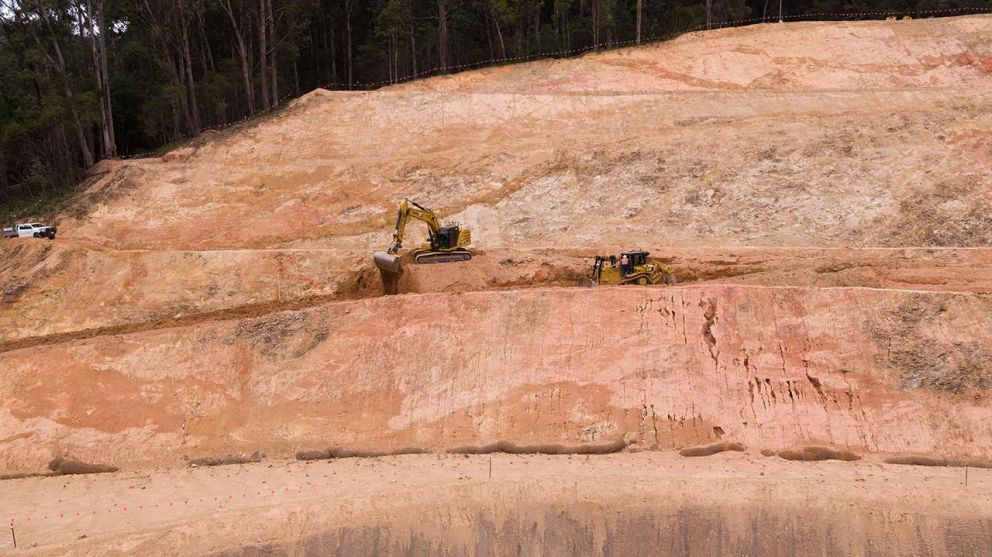 Machines moving earth to create large benches across the face of the landslip