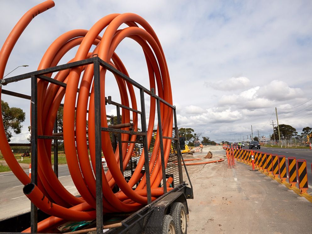 Image shows tubing positioned on a trailer and being laid onsite. To the right of the image is roadworks